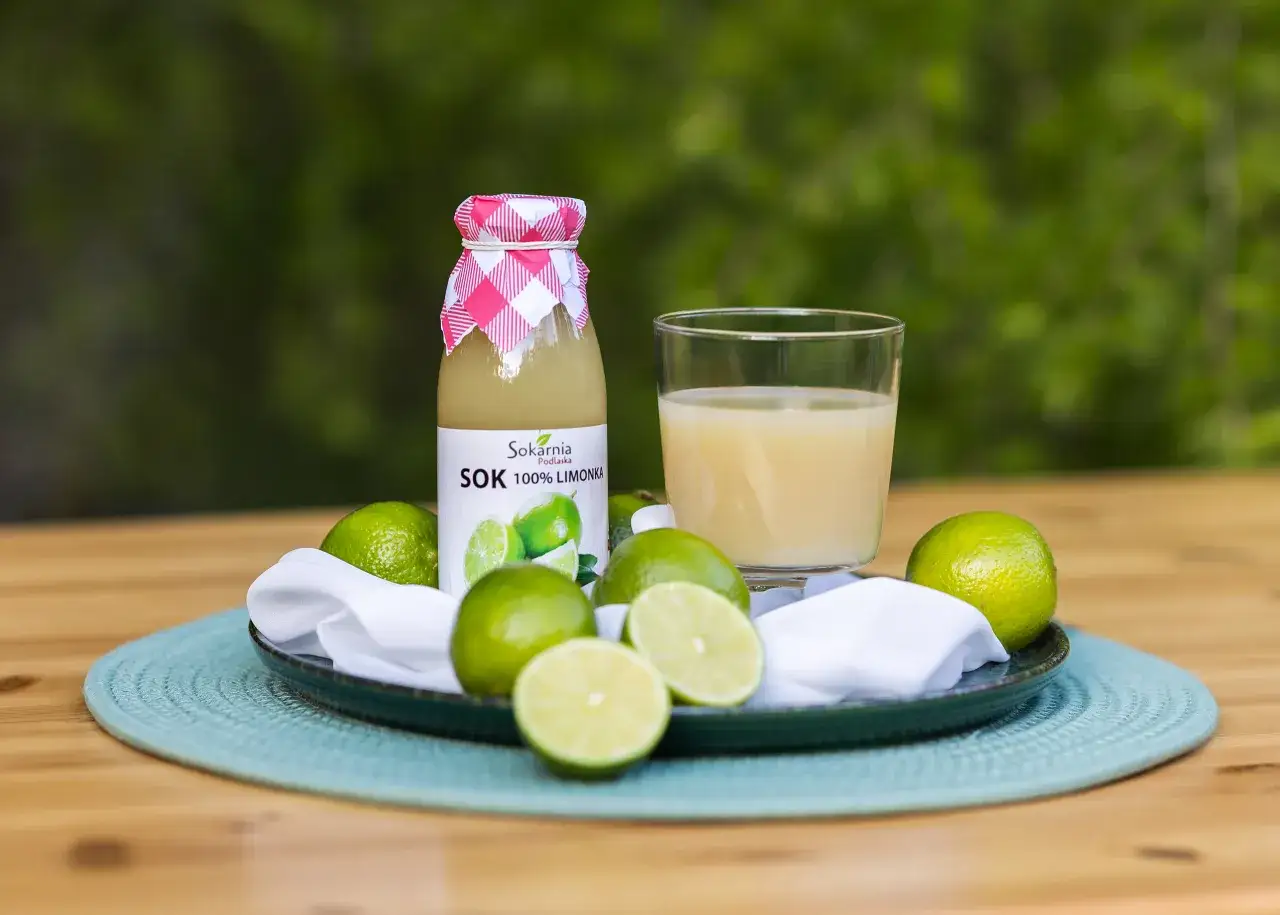 Butelka soku z limonki i szklanka orzeźwiającego napoju, otoczone świeżymi owocami. Odkryj sok z limonki właściwości!