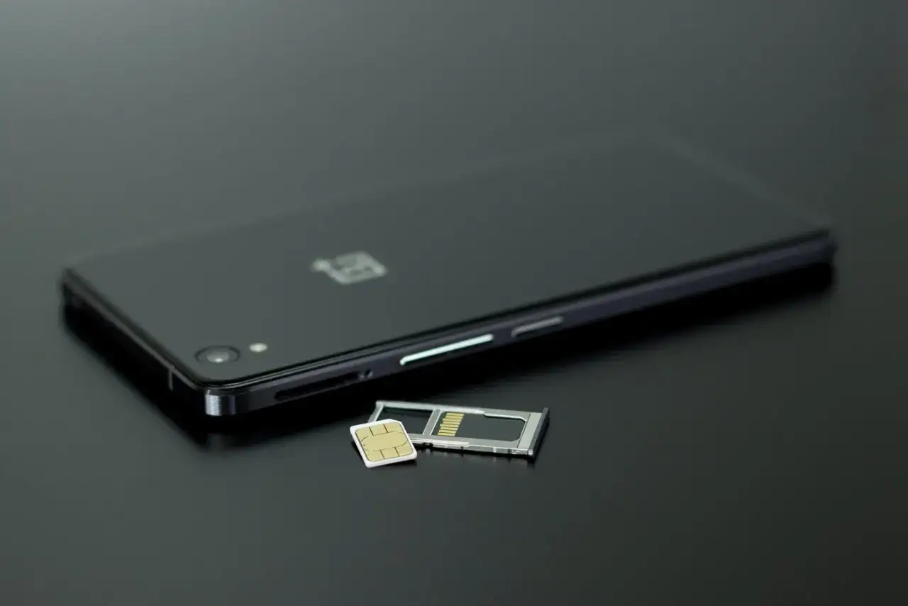 Czarny smartfon z tacką na kartę SIM i kartą pamięci obok. Dowiedz się, jak przenieść zdjęcia z telefonu na kartę pamięci.