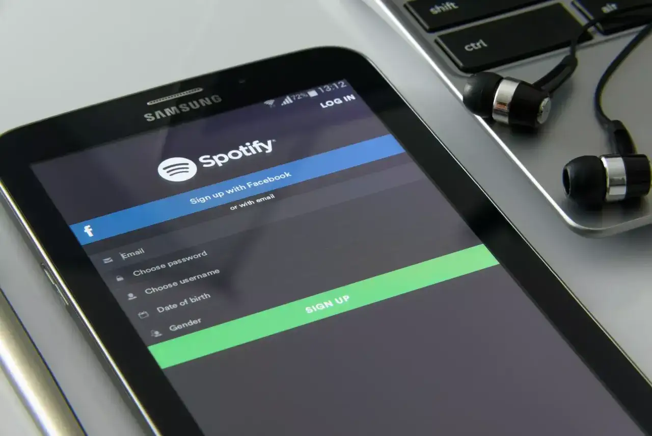 Ekran telefonu z aplikacją Spotify, formularzem rejestracji i słuchawkami na klawiaturze.