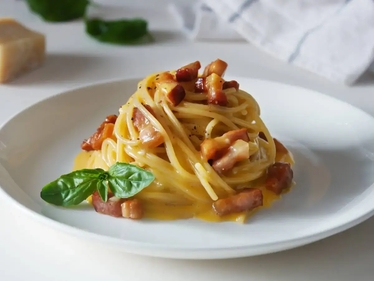 Spaghetti carbonara – przepis oryginalny ze śmietaną. Pyszne danie z makaronem, boczkiem i kremowym sosem jajeczno-serowym, udekorowane bazylią.