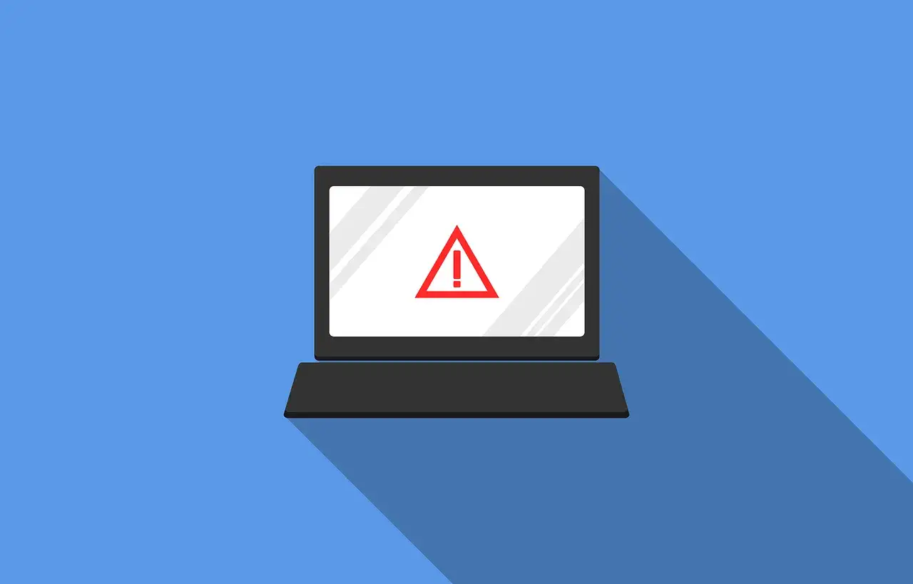 Laptop z czerwonym znakiem ostrzegawczym na ekranie. Symbolizuje zagrożenie w cyberbezpieczeństwie.