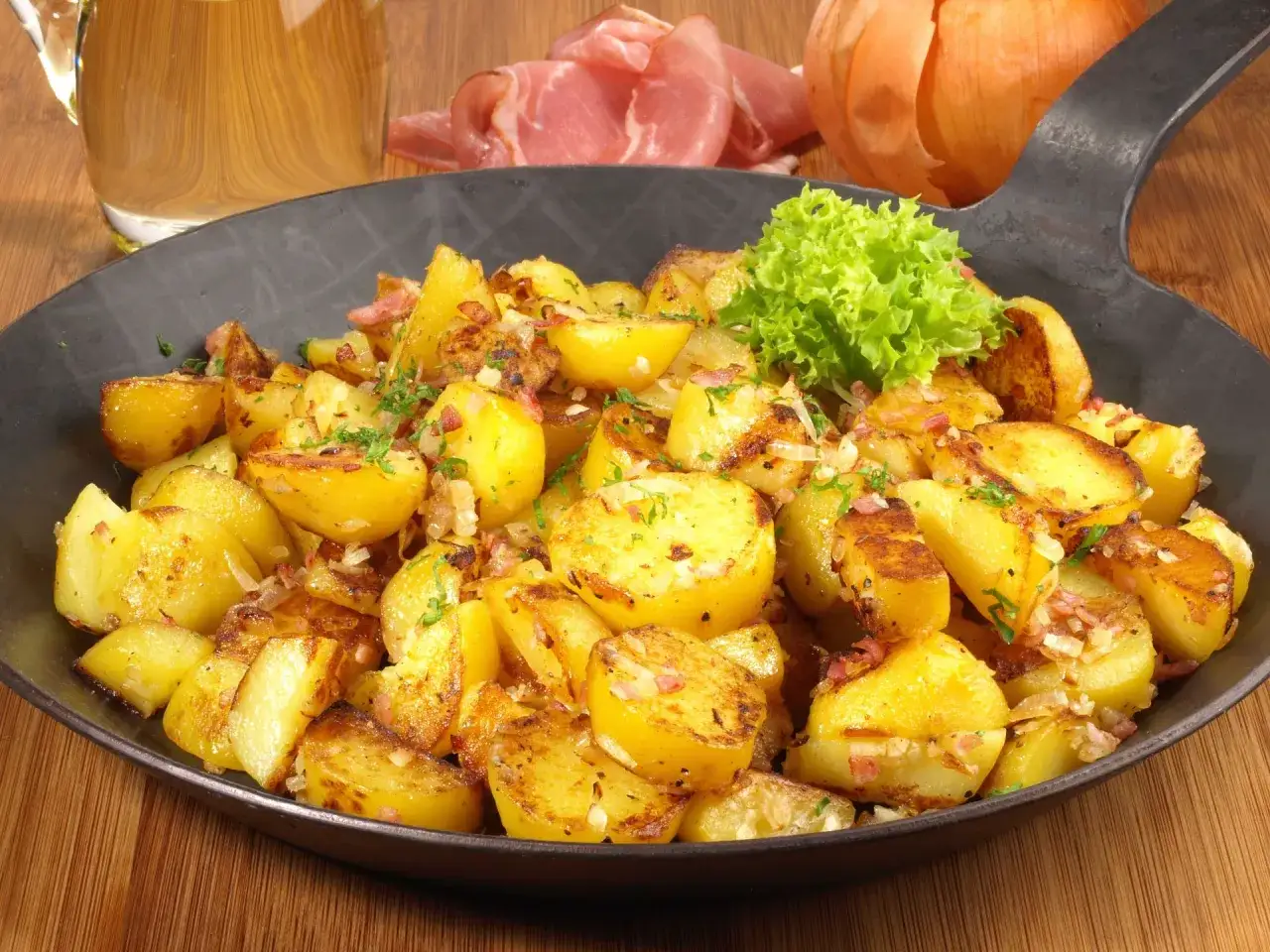 Goldbraune Bratkartoffeln mit Speck und Zwiebeln, garniert mit Petersilie. Ein klassisches Bratkartoffeln Rezept, serviert in einer Eisenpfanne.