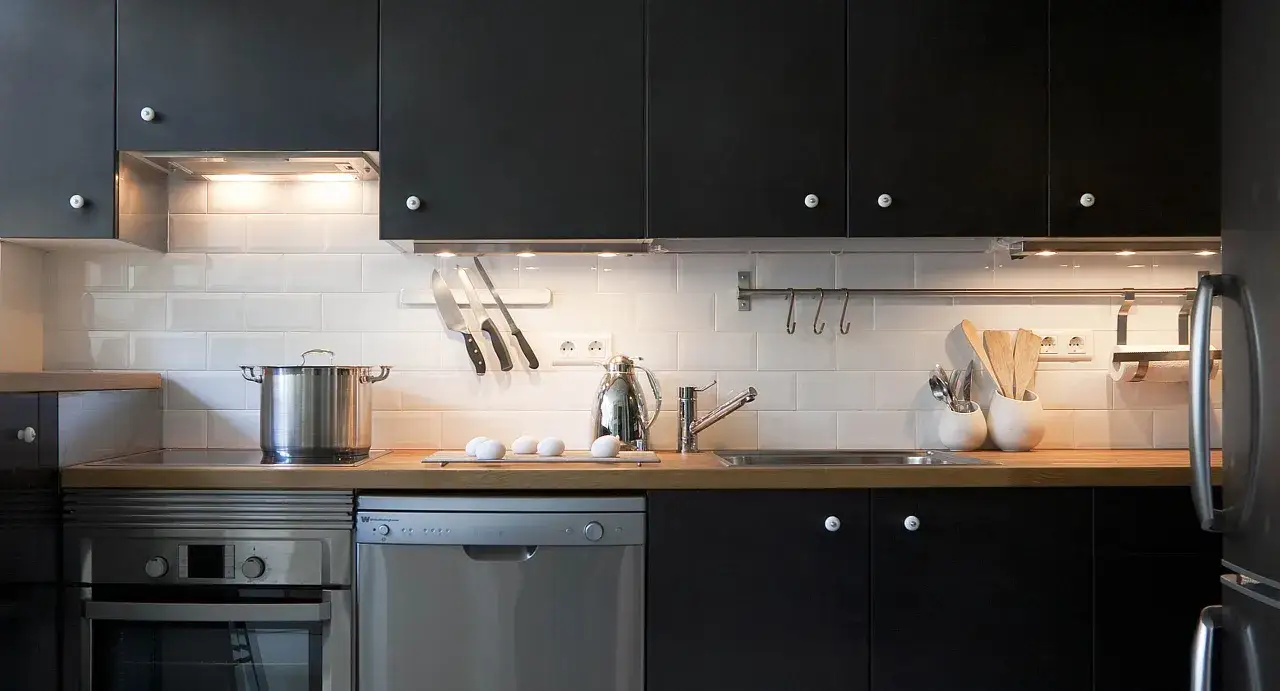 Cocinas en negro modernas con electrodomésticos de acero inoxidable, encimera de madera y azulejos blancos.