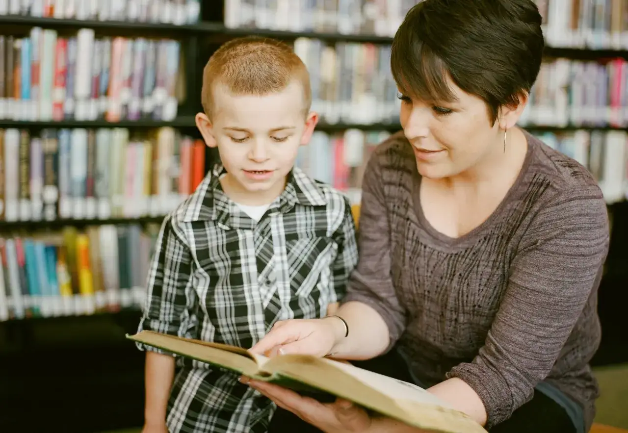 Kobieta i chłopiec czytają książkę w bibliotece. Pokazuje to, jak czytanie książek wpływa na człowieka, rozwijając wyobraźnię i wiedzę.