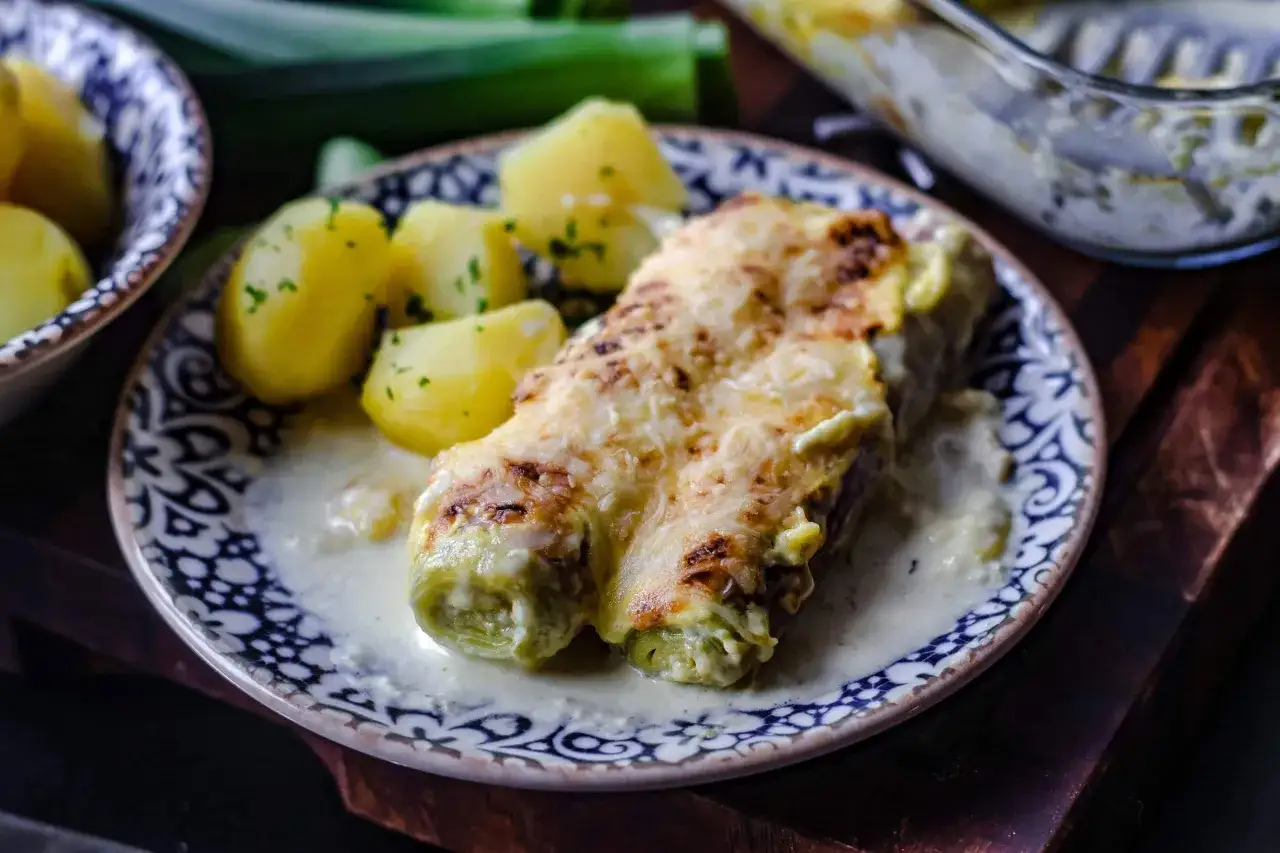 Gebackener Lauch mit Schinken, überbacken mit Käse, serviert mit Salzkartoffeln und einer cremigen Sauce.