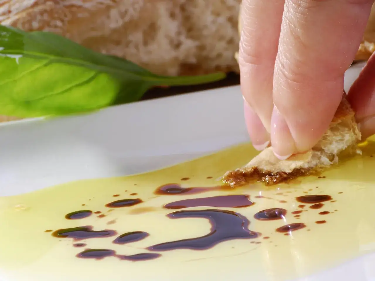 Ein Stück Brot wird in Olivenöl mit Balsamico getunkt. Eine Frau genießt diesen Snack, vielleicht während der Schwangerschaft.