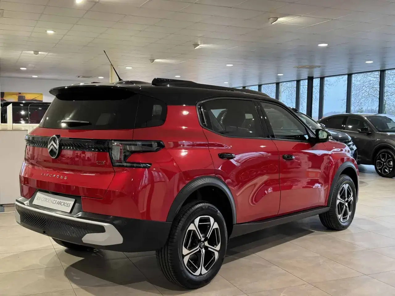 Błyszczący czerwony Citroën C3 Aircross z czarnym dachem stoi w salonie.
