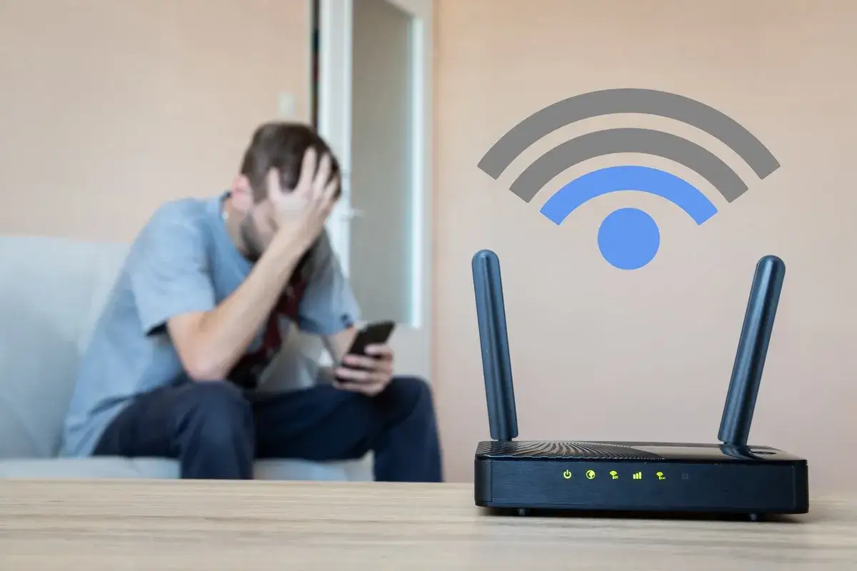 Un homme frustré regarde son téléphone, tandis qu'un routeur wifi est en premier plan. C'est quoi le wifi ? Une connexion sans fil essentielle.