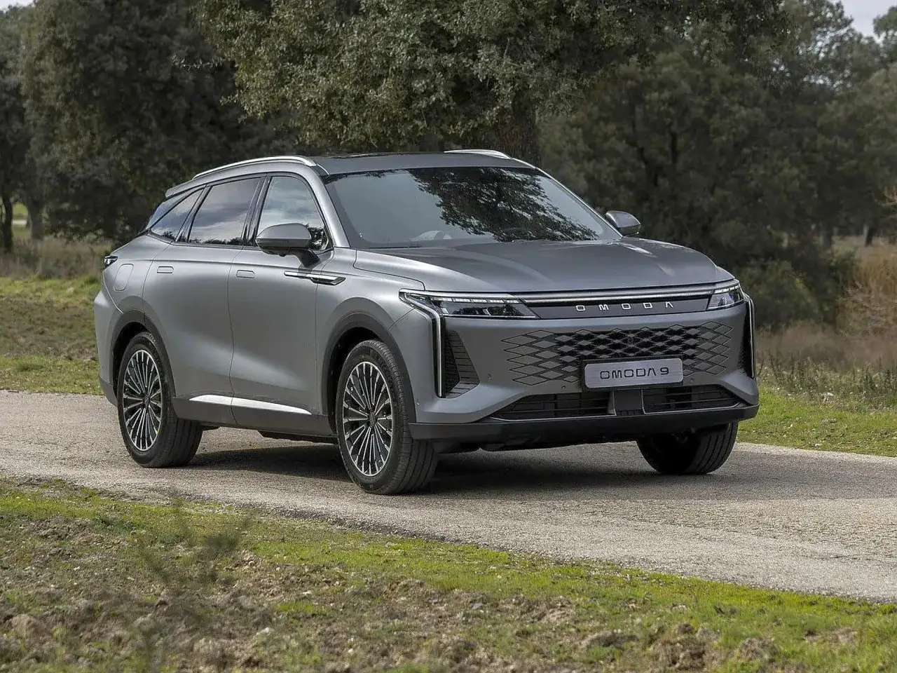 Szary OMODA 9 na drodze leśnej. Nowoczesny SUV z charakterystycznym grillem i światłami LED.