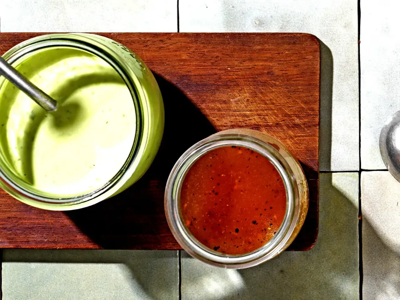 Zwei Gläser mit Saucen: ein cremiges Avocado Dressing für Salat und eine rote Vinaigrette.