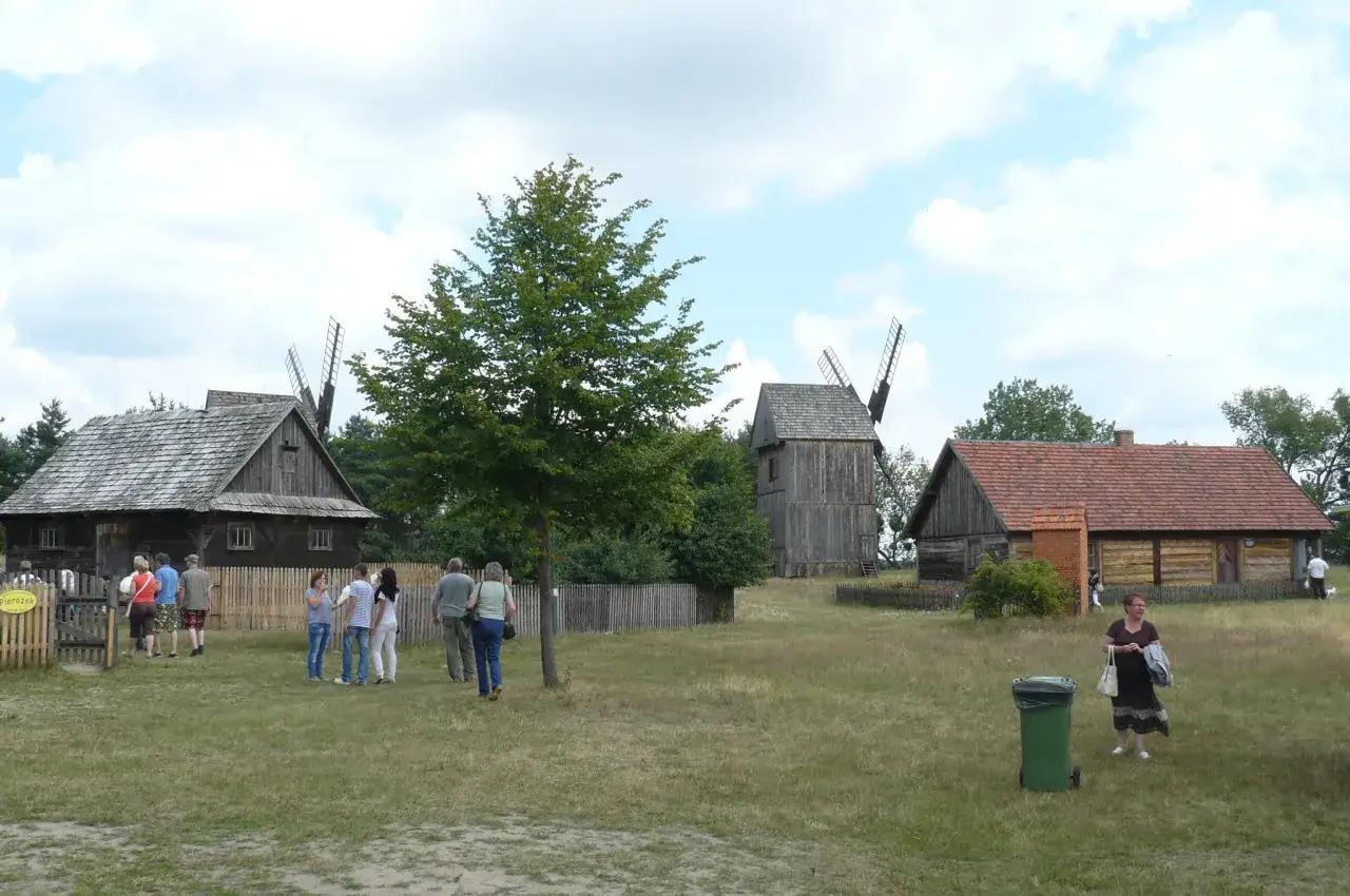 Skansen Osiek: drewniane budynki, wiatraki i ludzie spacerujący po trawie.