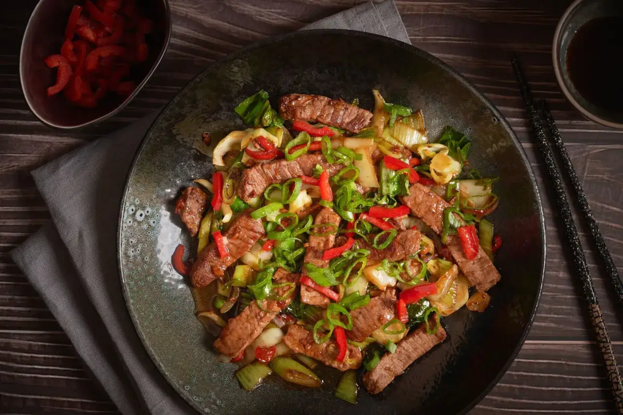 Pyszne wieprzowina w sosie teriyaki z papryką i szczypiorkiem, podana na ciemnym talerzu.