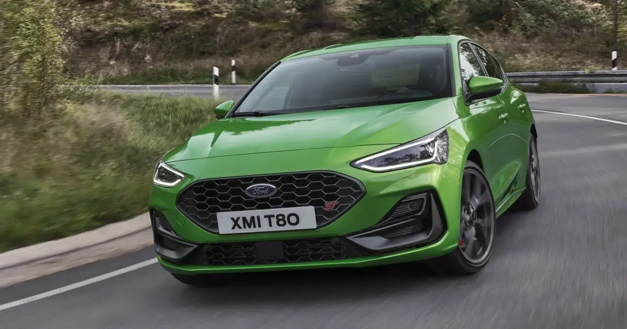 Jaskrawozielony Ford Focus 2025 ST z charakterystycznym grillem i światłami LED pokonuje zakręt na malowniczej, leśnej drodze.