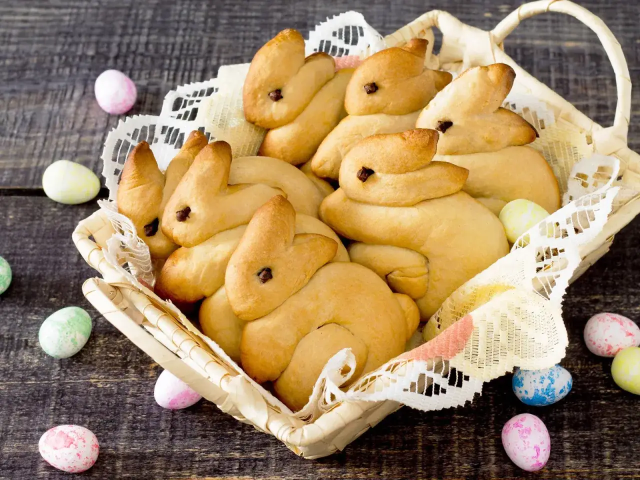 Korb voller goldbrauner Quark Osterhasen, umgeben von bunten Ostereiern auf dunklem Holz.