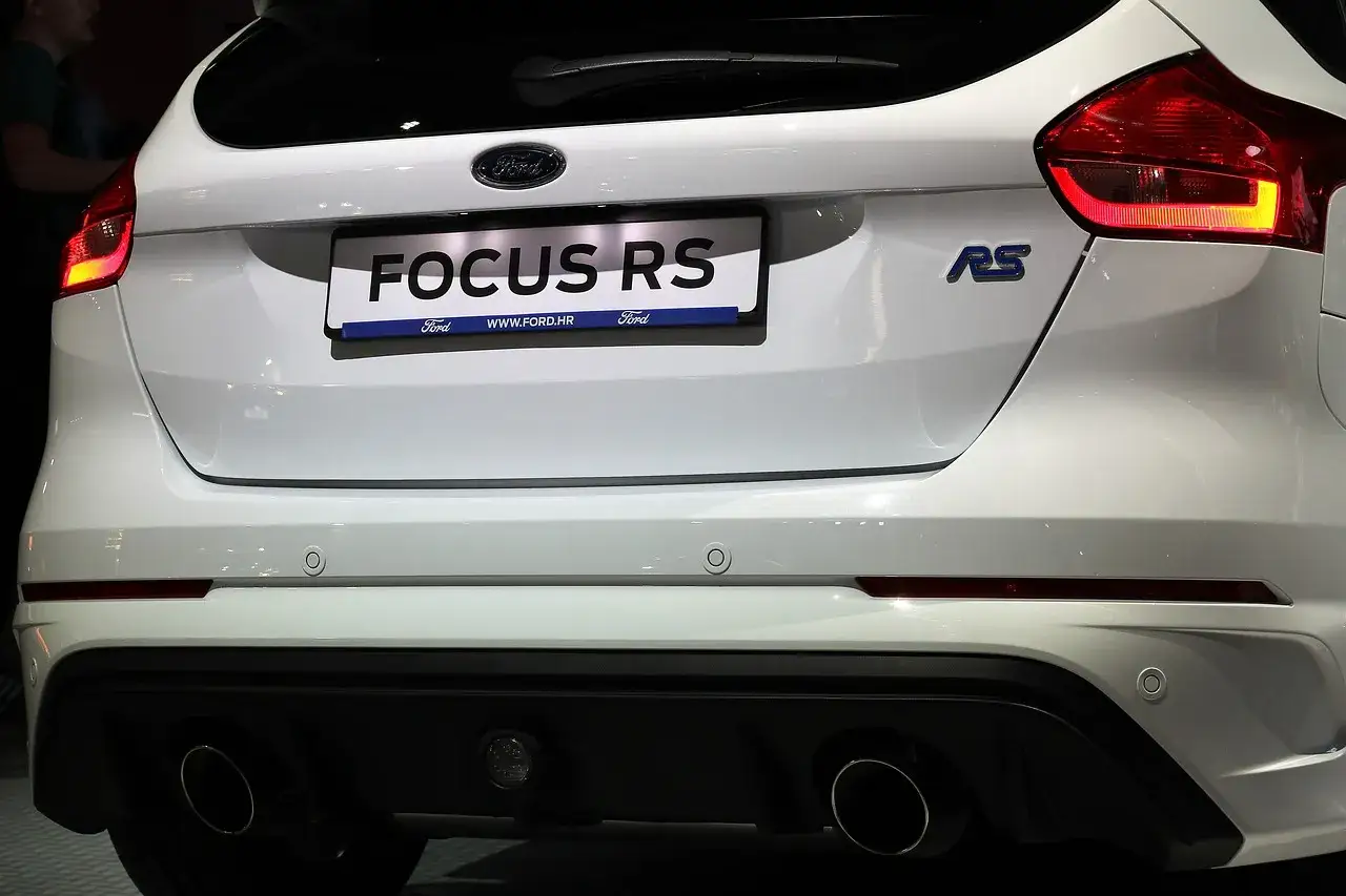 Biały Ford Focus RS z podwójnym wydechem i niebieskim znaczkiem RS.