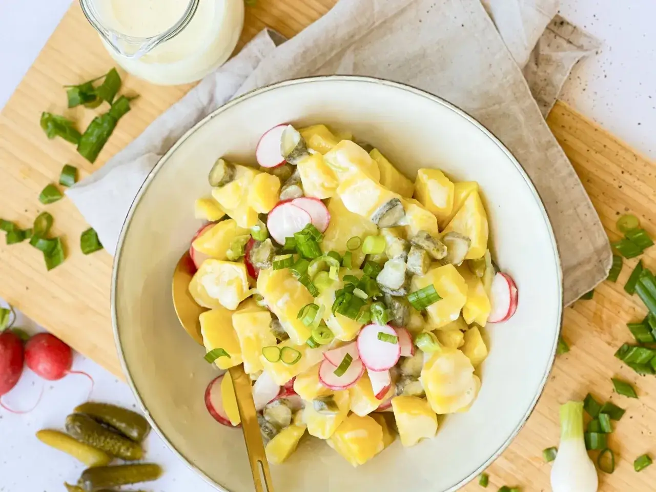 Ein cremiger veganer Kartoffelsalat mit Mayo, Radieschen und Gurken, garniert mit Frühlingszwiebeln.