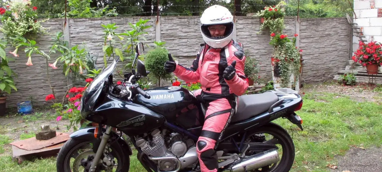 Niska dziewczyna w różowym kombinezonie motocyklowym i kasku siedzi na czarnym motocyklu Yamaha Diversion.