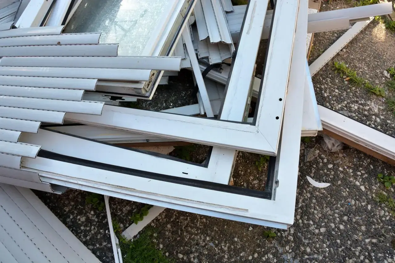 Stare okna PCV czekają na recykling. Widok pokazuje stos białych ram okiennych, niektóre z szybami, gotowe do przetworzenia.