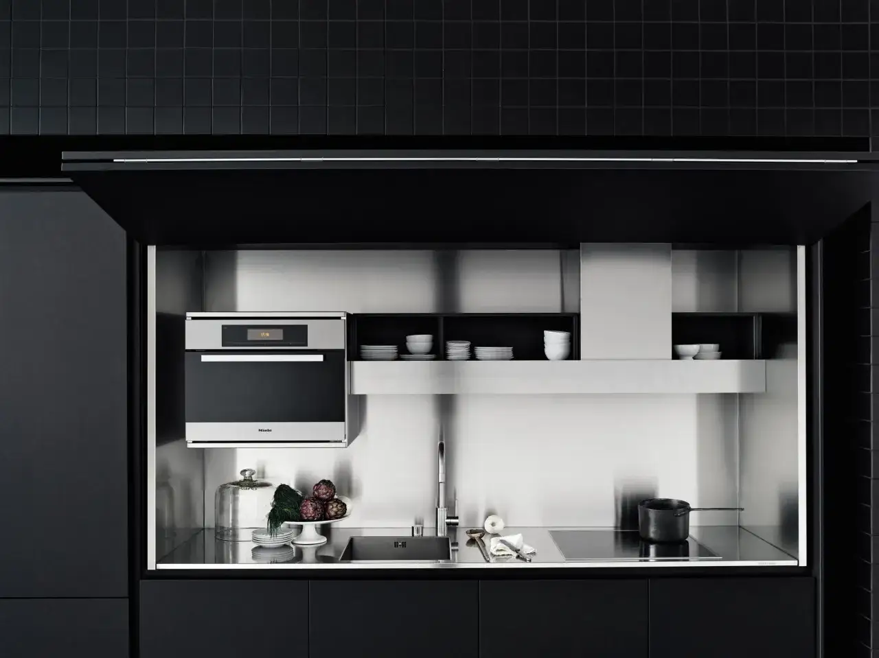 Cocinas invisibles: un horno Miele, fregadero y placa de inducción integrados en un diseño minimalista de acero inoxidable y gabinetes negros.