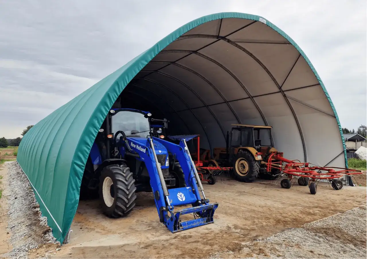 Zielona wiata bez pozwolenia wymiary chroni niebieski traktor New Holland i żółty traktor z maszynami rolniczymi.