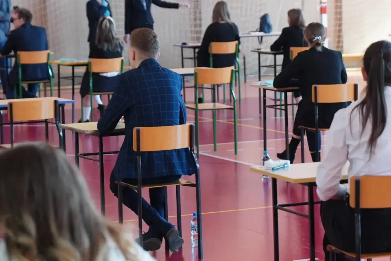 Uczniowie siedzą w ławkach na sali gimnastycznej, skupieni na zadaniach. To moment, kiedy sa matury, a przyszłość wielu zależy od tych egzaminów.
