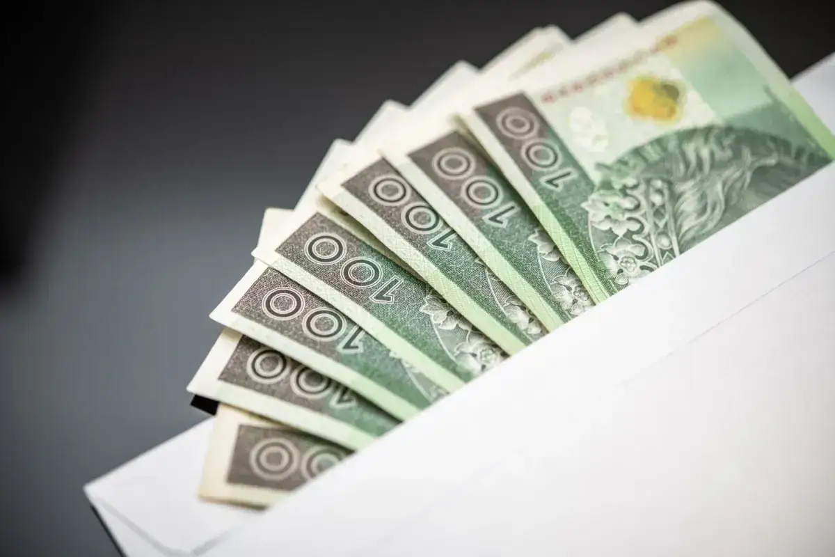 Banknoty 100 zł w kopercie. Symbol jawności wynagrodzeń i transparentności finansowej.