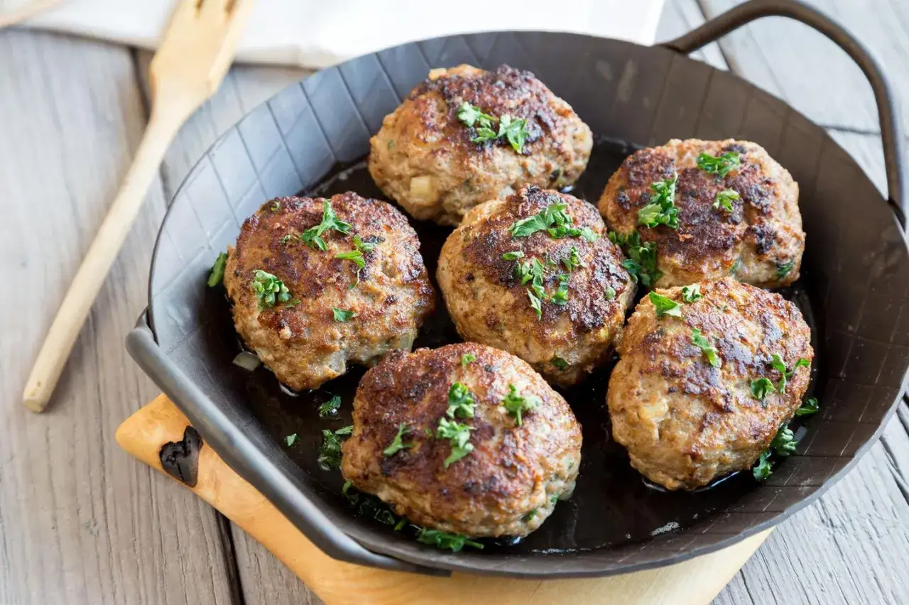 Sechs goldbraune Fleischpflanzerl, garniert mit Petersilie, in einer Pfanne. Ein leckeres Fleischpflanzerl Rezept zum Nachkochen.