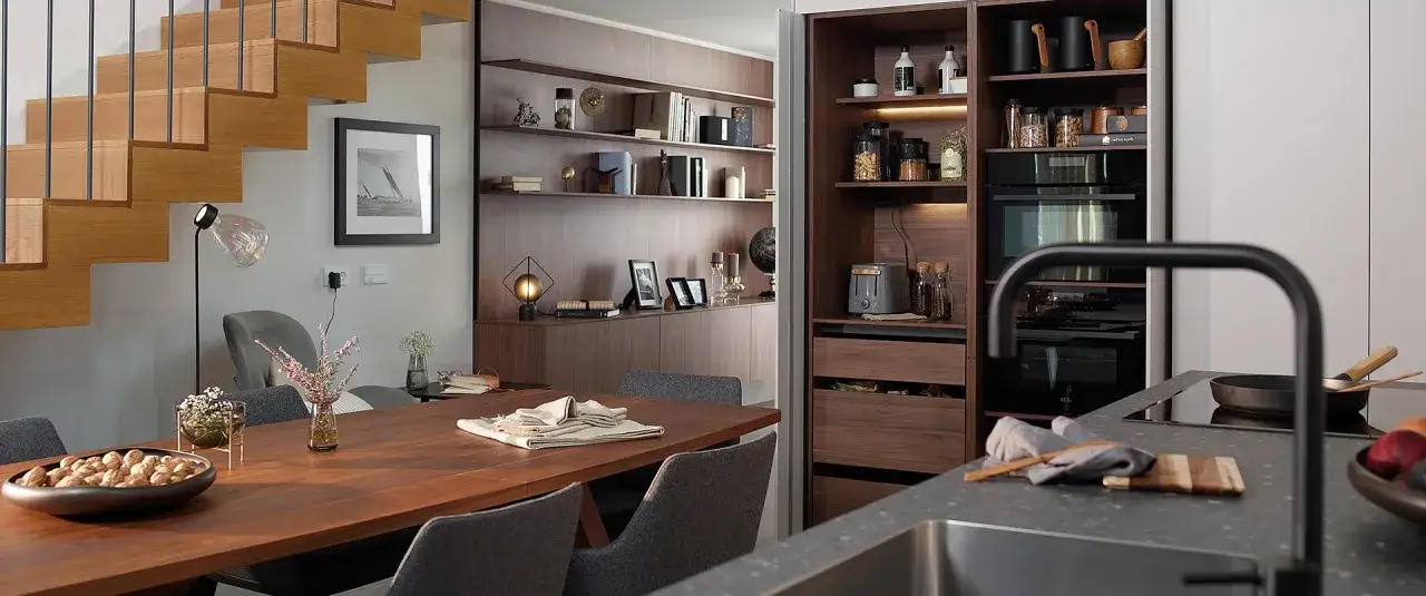 Comedor y zona desayuno cocina con mesa de madera, sillas grises y estanterías empotradas.