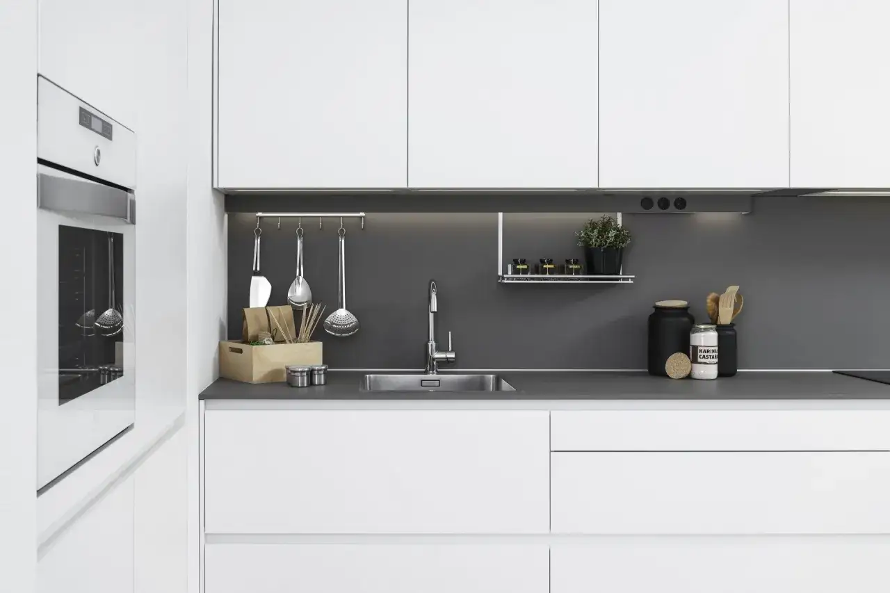 Moderna cocina blanca y gris con electrodomésticos integrados, fregadero de acero inoxidable y utensilios de cocina colgados.
