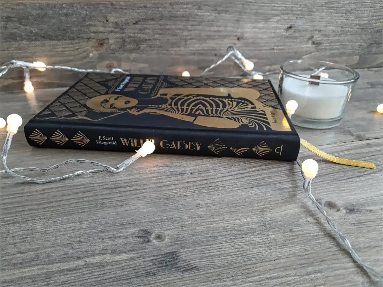Książka "Wielki Gatsby" F. Scotta Fitzgeralda, otoczona świątecznymi lampkami, zaprasza do odkrycia jej streszczenia i historii.