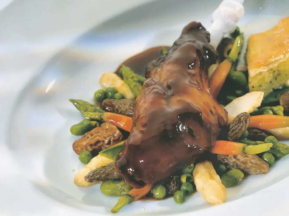 Ein köstliches Kaninchen-Rezept: zartes Kaninchenfleisch in dunkler Sauce, serviert mit Spargel, Erbsen, Karotten und Morcheln.