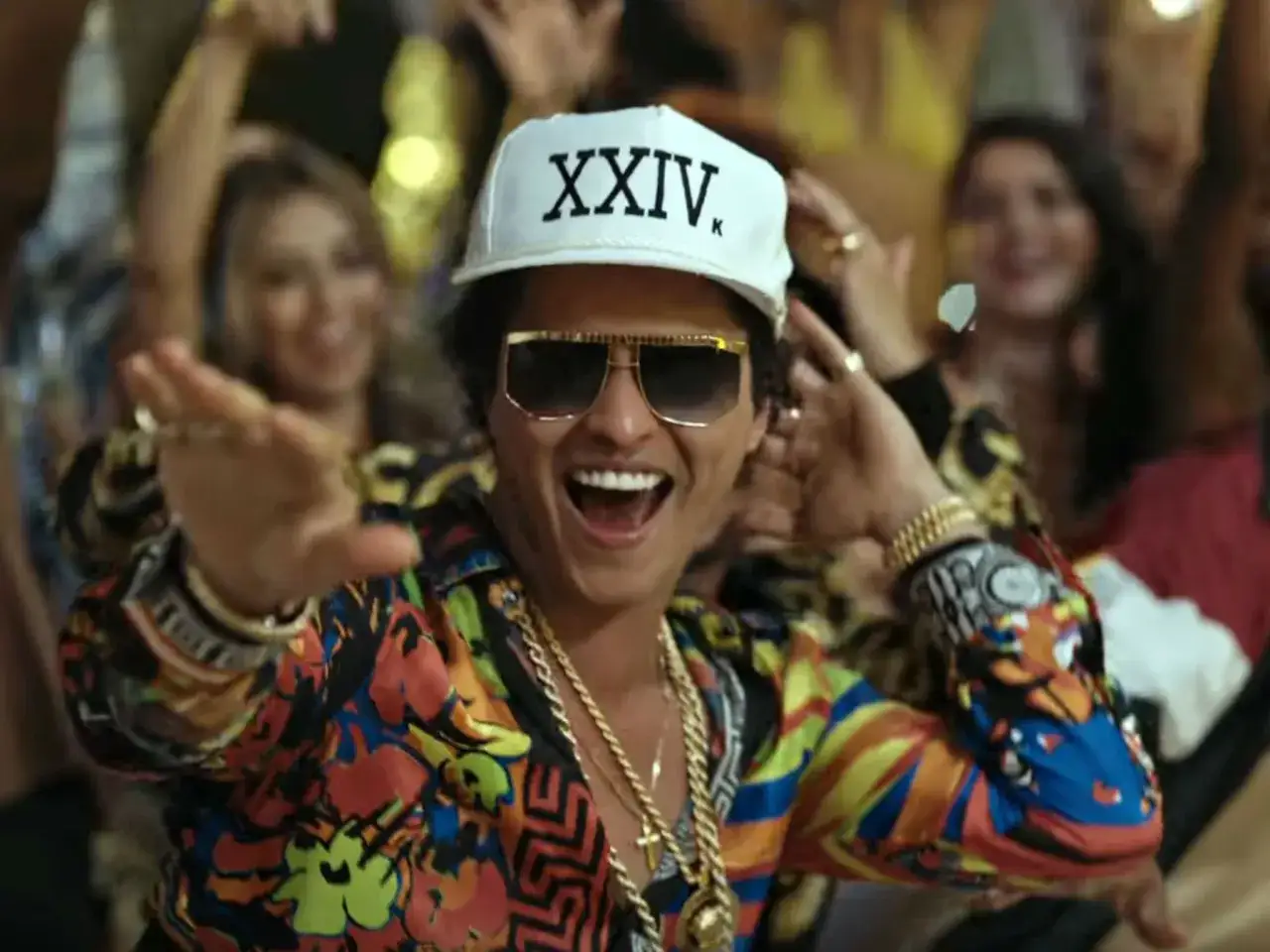 Bruno Mars w Polsce! Wesoły artysta w kolorowej koszuli i czapce z napisem "XXIV K" tańczy wśród rozbawionych ludzi.