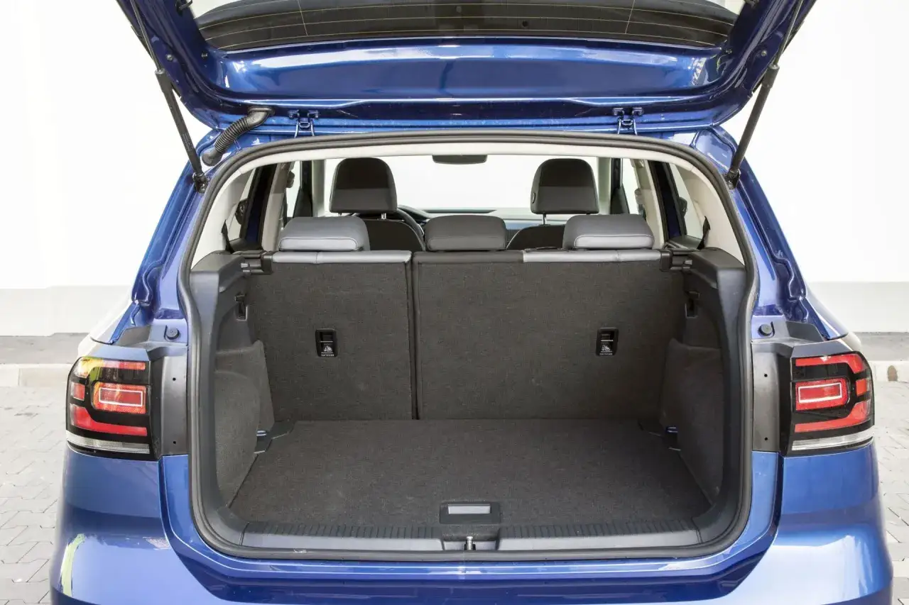 Błękitny Volkswagen T-Cross z otwartym bagażnikiem. Widać tylne siedzenia i przestronną przestrzeń bagażową, idealną na wakacyjne wyjazdy.