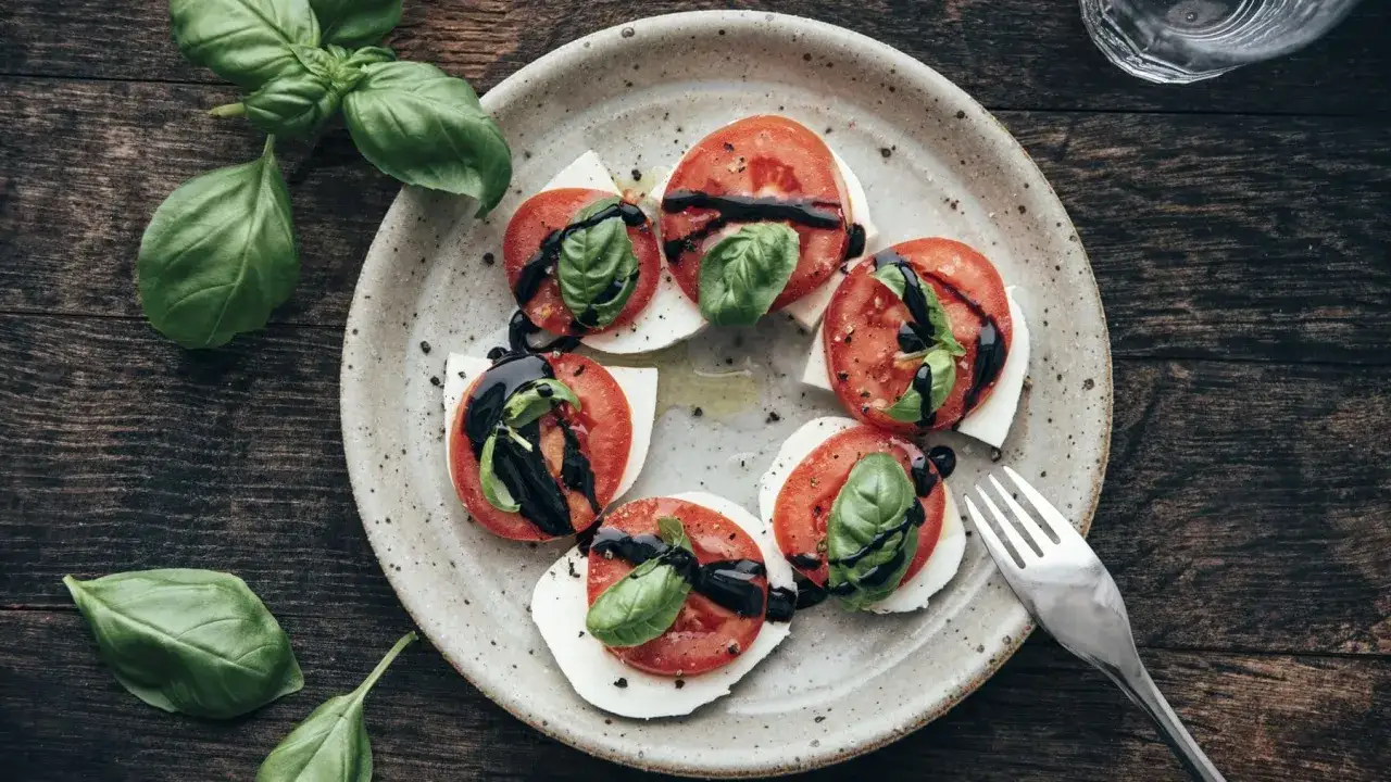 Tomate-Mozzarella-Salat mit frischem Basilikum und Balsamico-Glasur auf einem rustikalen Teller.
