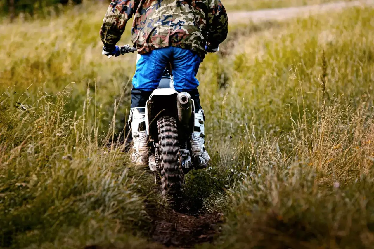 Motocyklista w stroju off-roadowym jedzie po trawiastym torze.