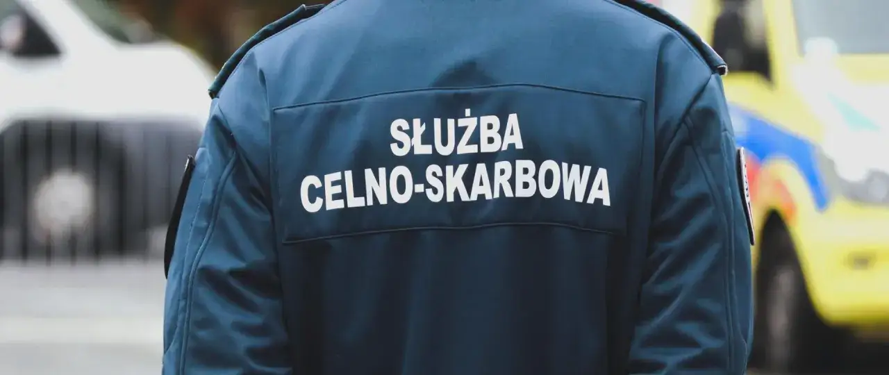Celnik w granatowej kurtce z napisem "SŁUŻBA CELNO-SKARBOWA" stoi obok pojazdu.