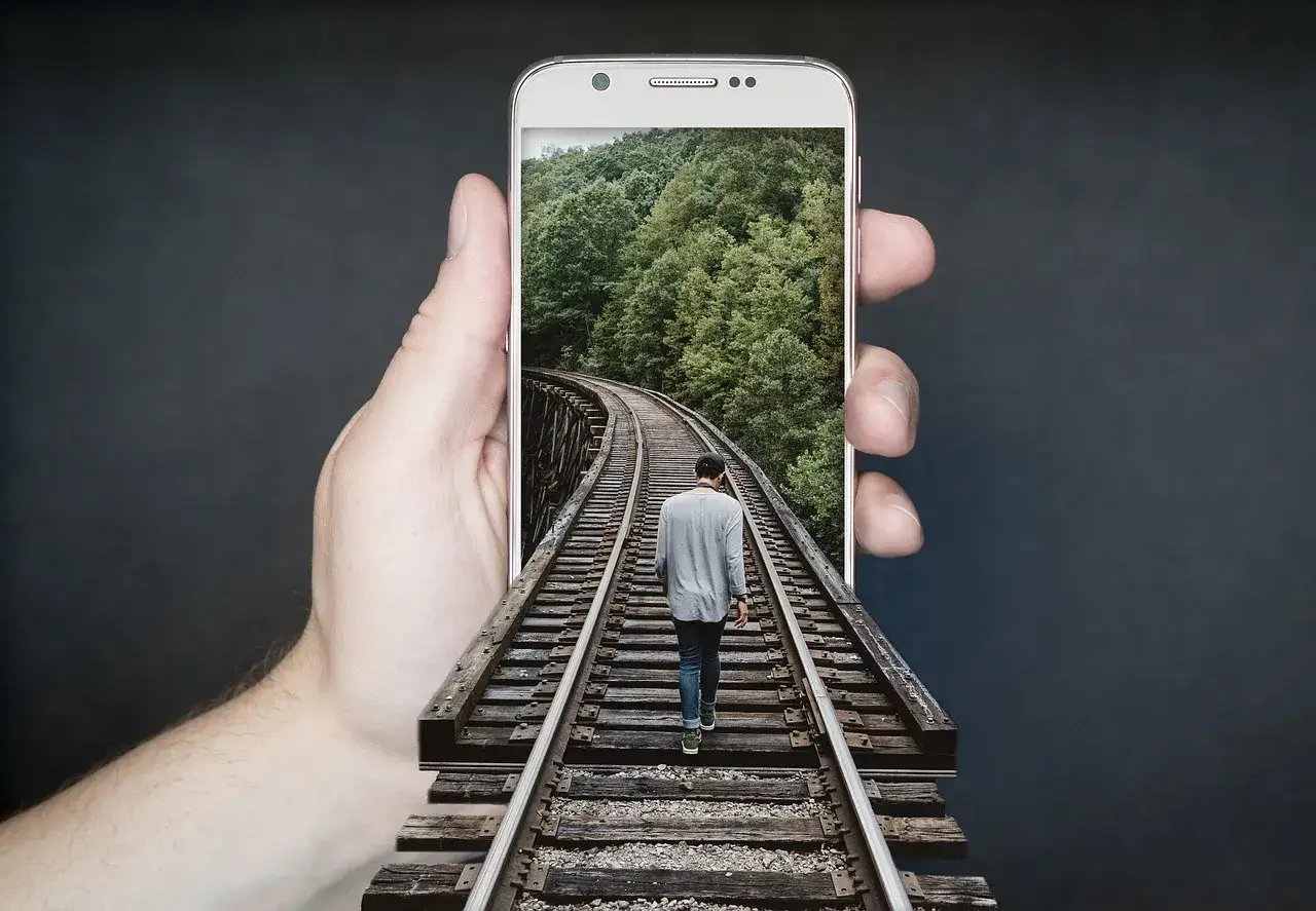 Dłoń trzyma telefon z ekranem **amoled**, na którym widać mężczyznę idącego po torach kolejowych przez las.