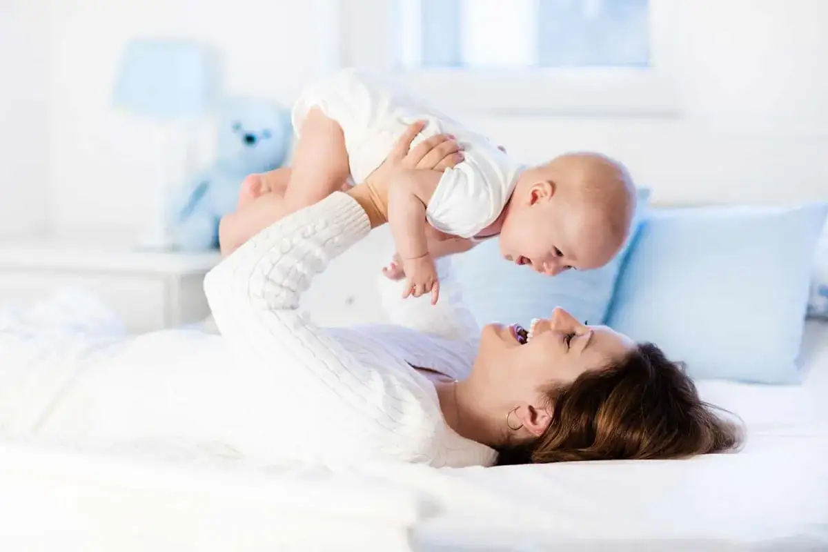 Szczęśliwa mama podrzuca dziecko, zastanawiając się, ile kosztuje opieka nad dzieckiem za godzinę.
