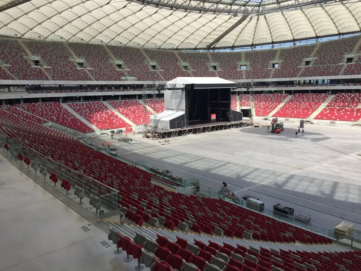 Przygotowania do koncertu Depeche Mode w Warszawie. Ogromny stadion z pustymi czerwonymi trybunami i sceną w budowie.