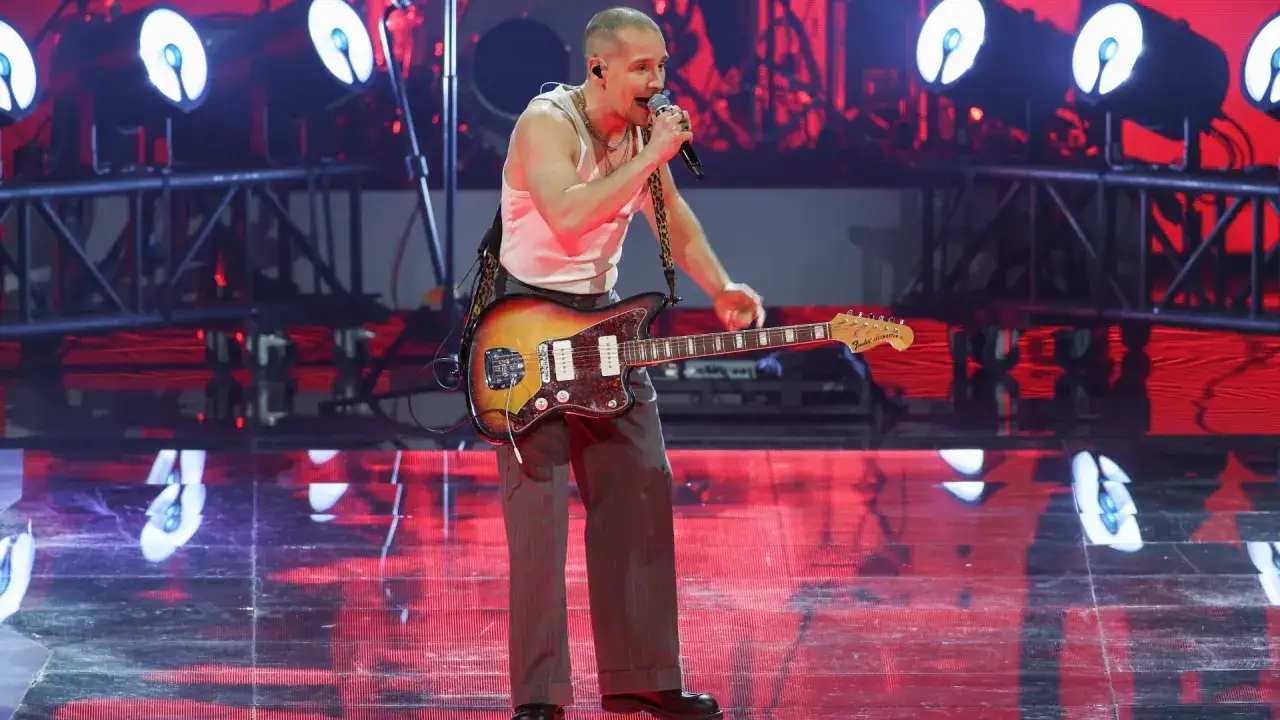 Krzysztof Zalewski na koncercie, śpiewa i gra na gitarze. Scena oświetlona czerwonymi światłami.