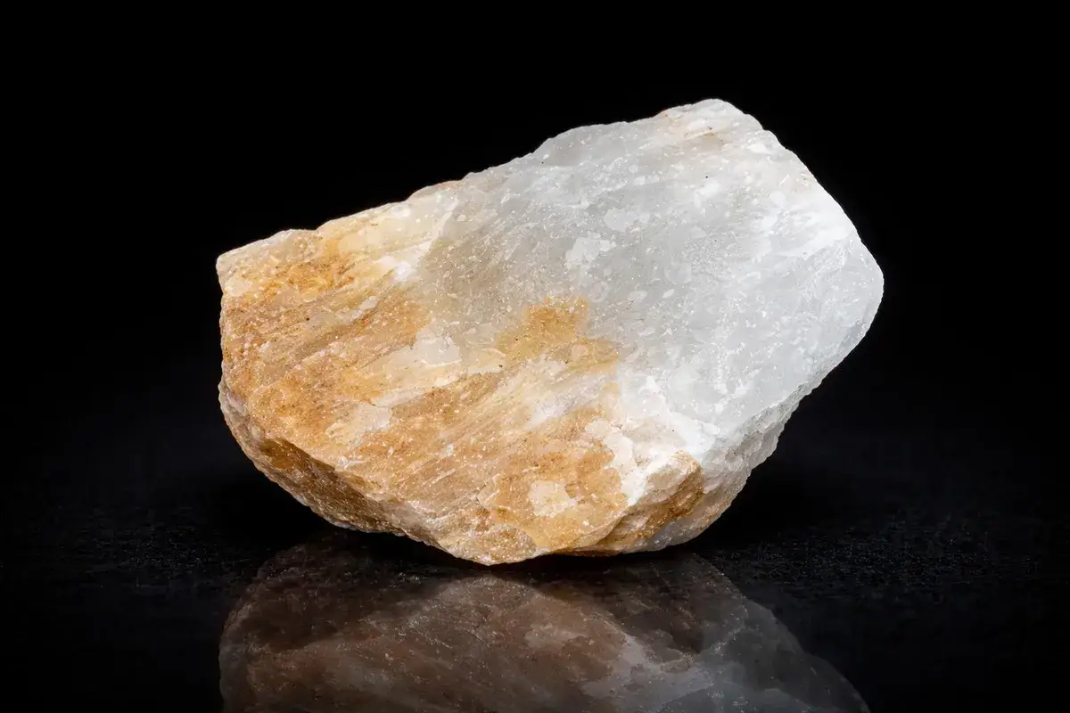 Ein Stück Alabaster, dessen Bedeutung in seiner Reinheit und seinem sanften Glanz liegt, schimmert in Weiß und Beige vor schwarzem Hintergrund.