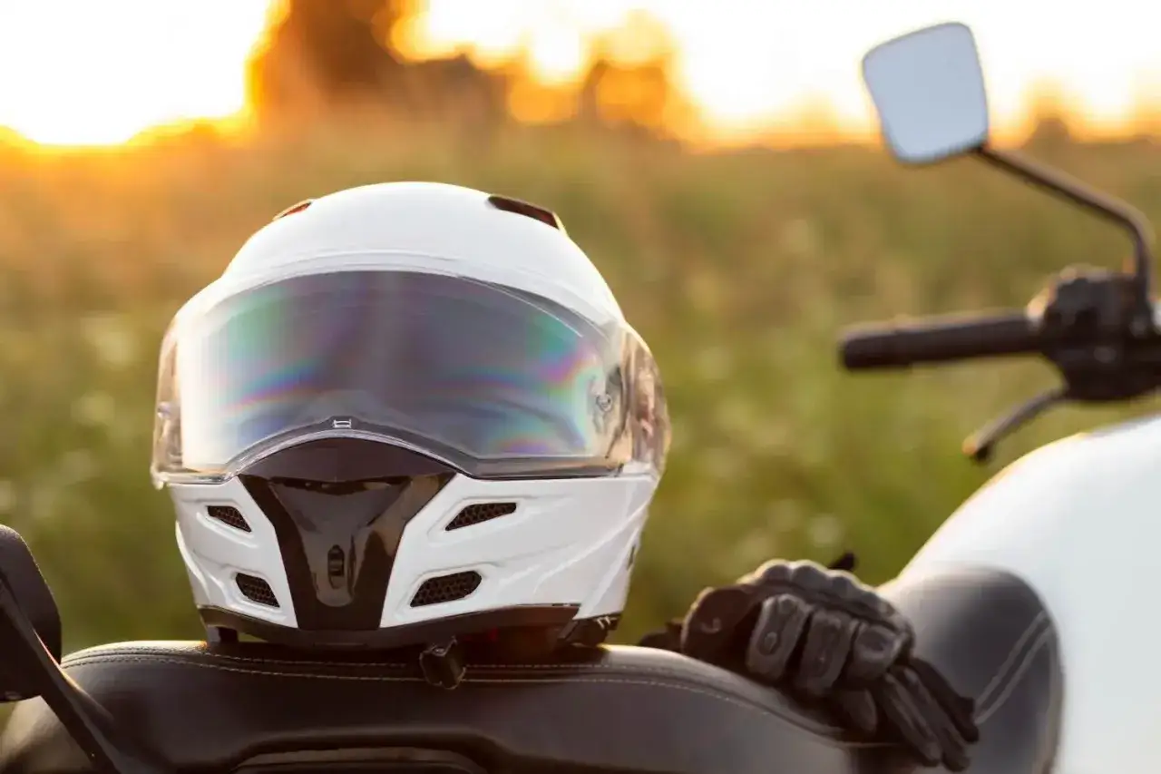 Biały kask motocyklowy i rękawice na siedzeniu motocykla podczas zachodu słońca.