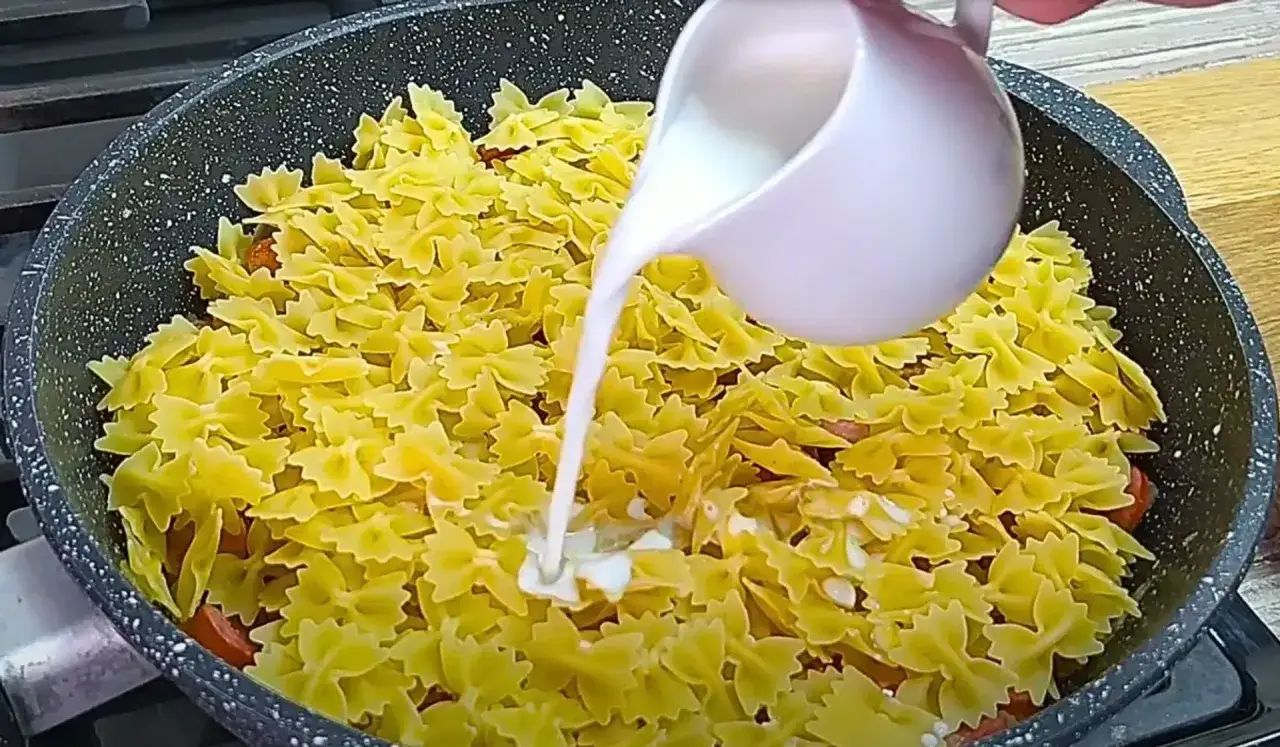 Makaron farfalle z kiełbasą w sosie śmietanowym, gotowany na patelni.