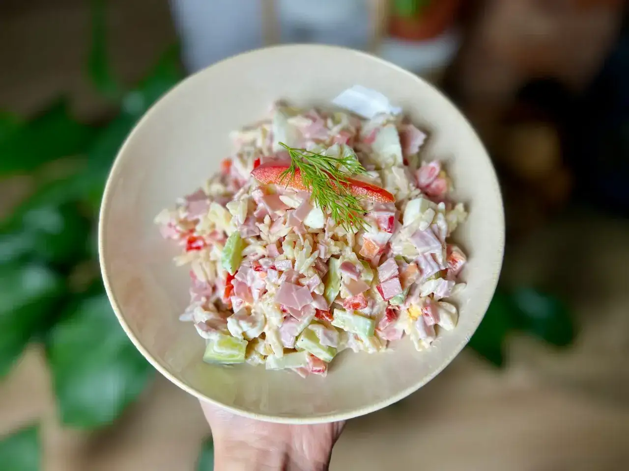 Pyszna sałatka z makaronem orzo, z szynką, jajkiem i warzywami, udekorowana gałązką koperku.