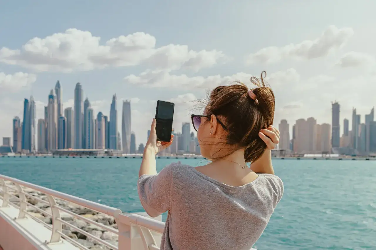 Kobieta robi zdjęcie telefonem na tle Dubaju. Zastanawia się, czy podatek w Dubaju wpłynie na jej wakacje.