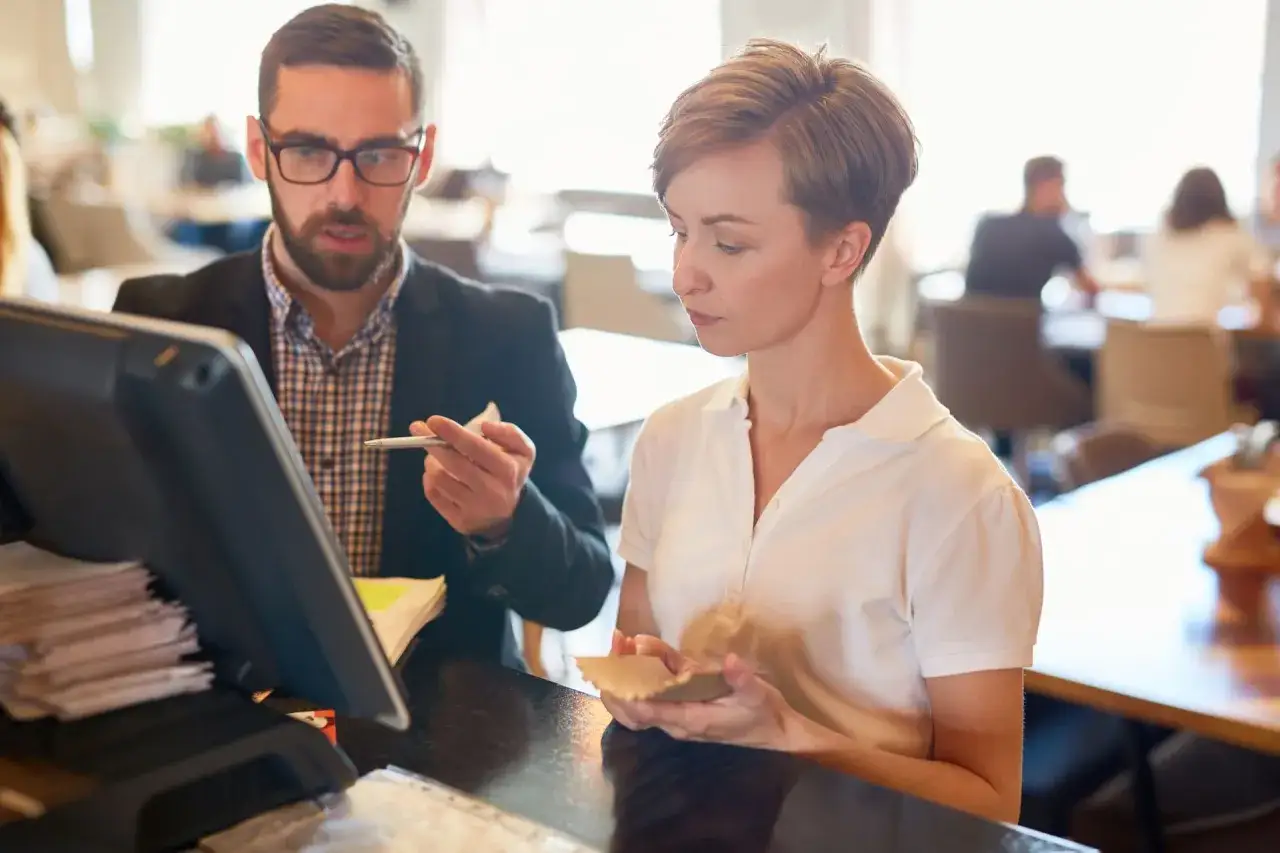 Mann mit Brille und Frau besprechen etwas am Kassensystem in einem Restaurant.