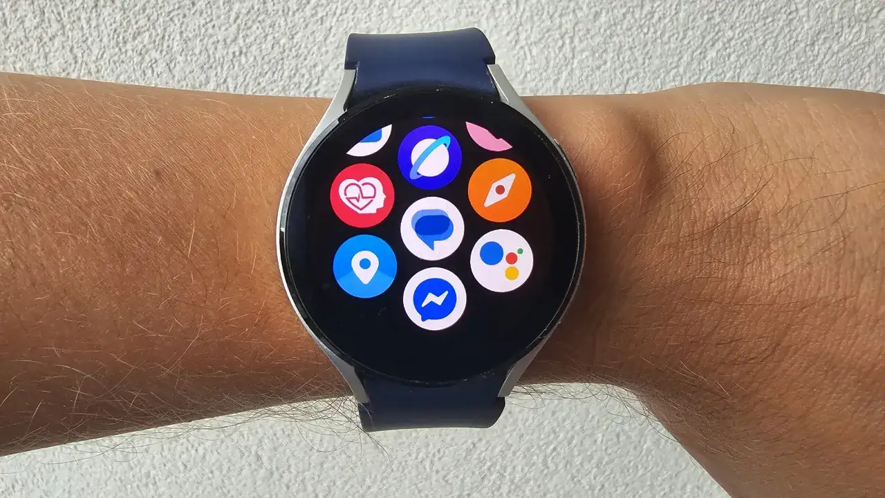 Zegarek z systemem Wear OS na nadgarstku, z widocznymi ikonami aplikacji: serce, lokalizacja, Messenger, Google Assistant i inne.
