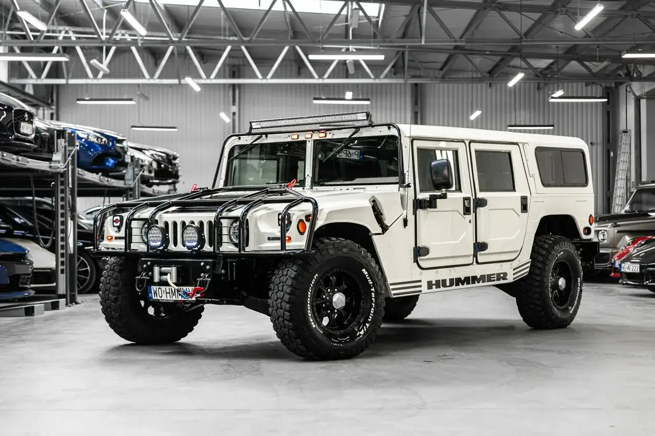 Biały Hummer H1 z potężnymi oponami i dodatkowym oświetleniem na dachu, gotowy na każdą przygodę.
