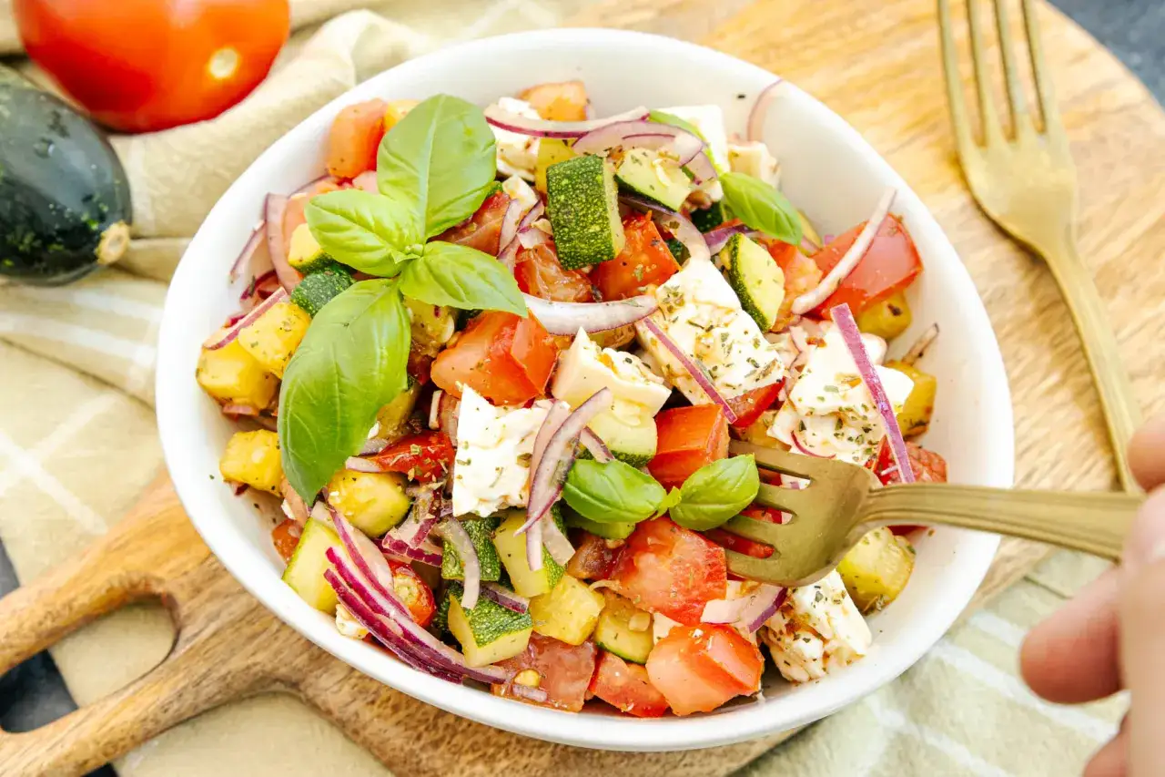 Frischer zucchini-salat mit feta, Tomaten, roten Zwiebeln und Basilikum, garniert mit Kräutern.