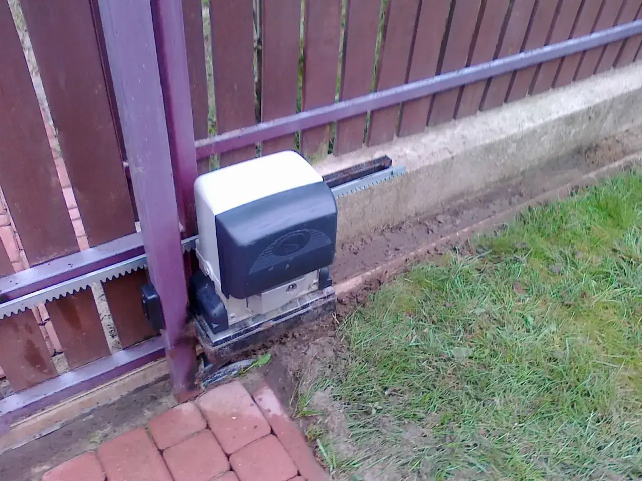 Silnik bramy przesuwnej, która po zamknięciu sama się otwiera, z widocznym zębatką i mechanizmem.